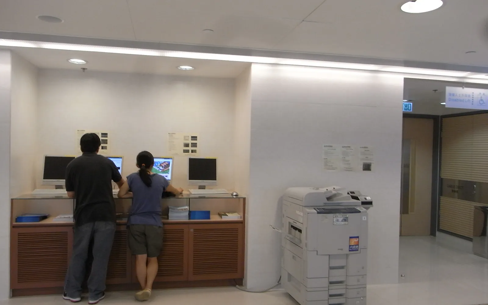 A shared office printer placed in an open area near computer workstations